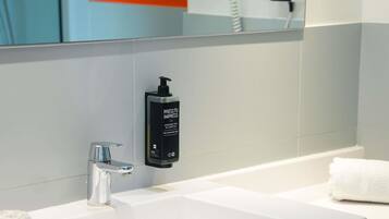A modern bathroom with a white sink, chrome faucet, and a black bottle dispenser labeled 'PRESS TO IMPRESS.'