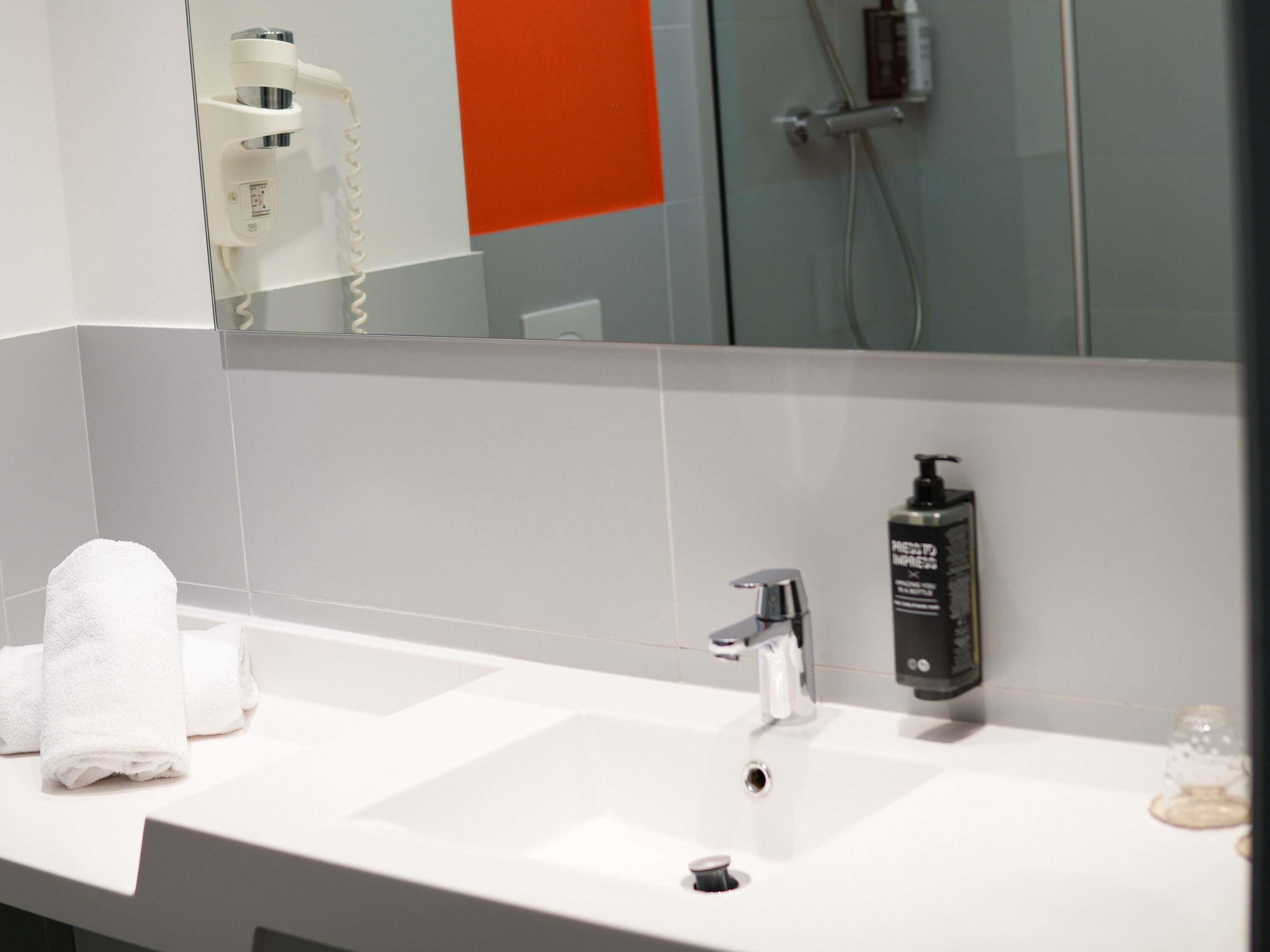 A bathroom with a white sink, a mirror, a towel, and a bottle of shampoo.