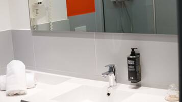 A bathroom with a white sink, a mirror, a towel, and a bottle of shampoo.