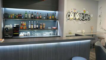 Zona de bar con diversas bebidas, una máquina de café y una pared con un cartel de wifi gratuito.