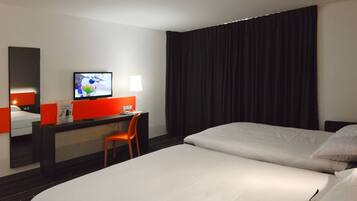 A hotel room with a bed, a desk with a chair, a television, and a window with curtains.