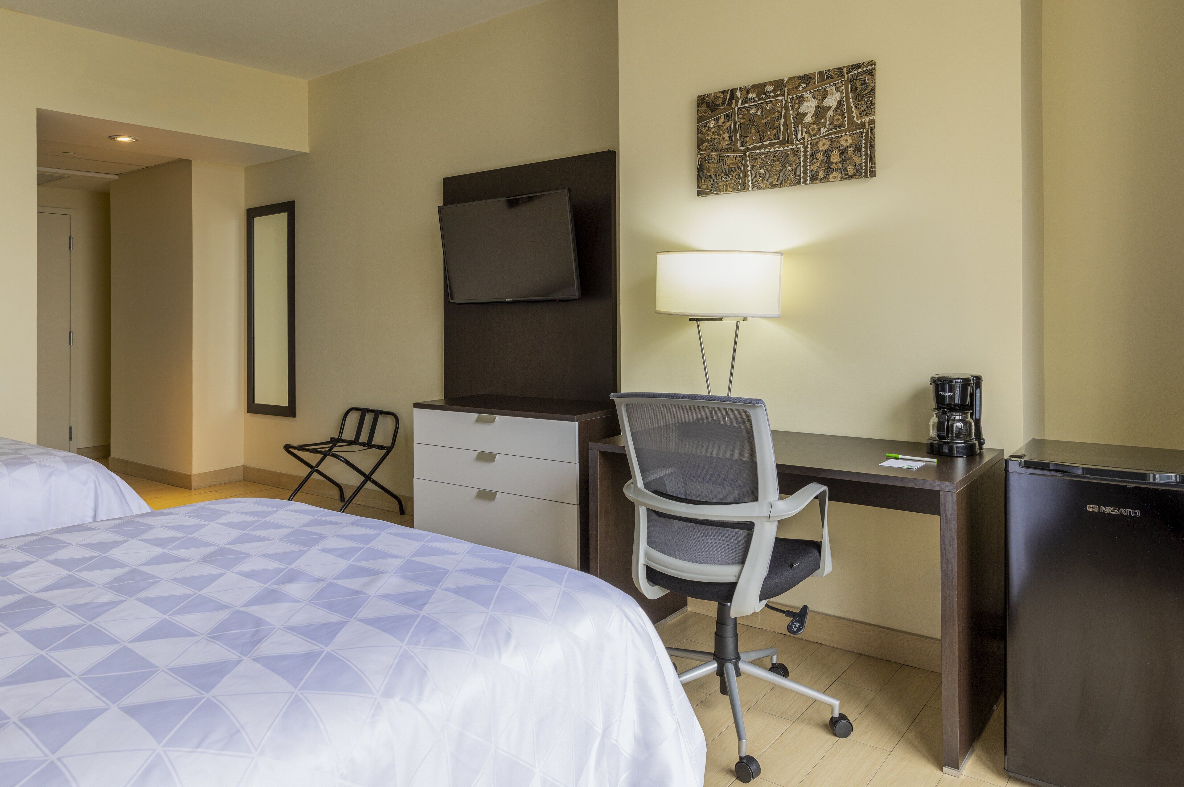A hotel room with a bed, a desk, a chair, a television, a coffee maker, and a refrigerator.
