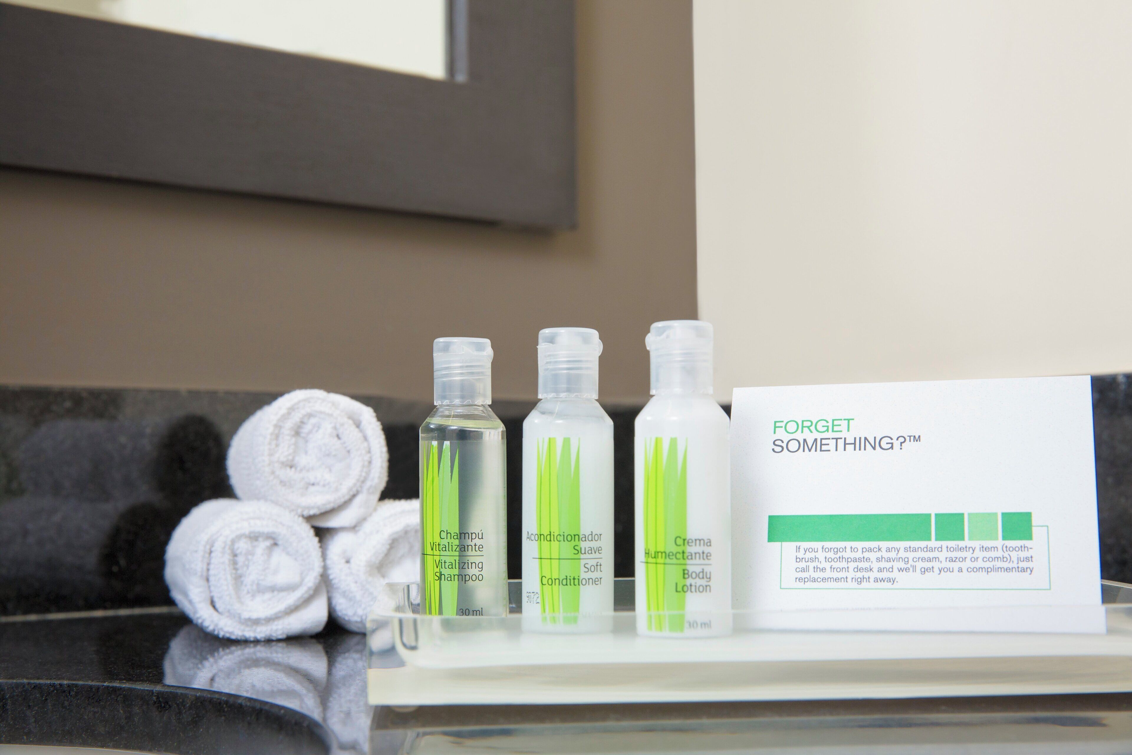 Toiletries including shampoo, conditioner, and body lotion on a counter with a sign offering complimentary replacements.