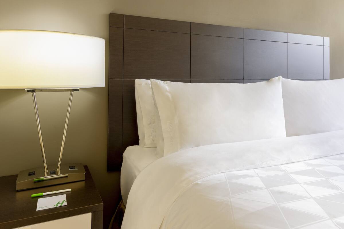 A neatly made bed with white linens, a modern lamp on a bedside table, and a headboard with a geometric pattern.