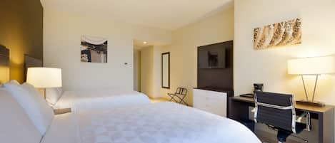 Habitación de hotel con dos camas, un escritorio, una silla, un televisor y obras de arte en las paredes.