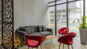 Ein modernes Interieur mit einem grauen Sofa, roten Stühlen, einem Holztisch und einem großen Fenster mit Blick auf die Straße.