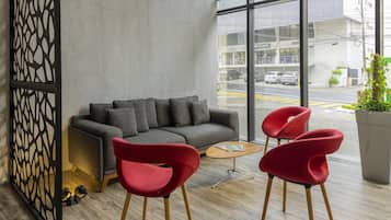 Ein modernes Interieur mit einem grauen Sofa, roten Stühlen, einem Holztisch und einem großen Fenster mit Blick auf die Straße.