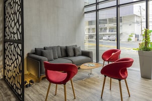 Un interior moderno con un sofá gris, sillas rojas, una mesa de centro de madera y un amplio ventanal con vistas a la calle.