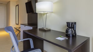Ein Hotelzimmer mit Schreibtisch, Stuhl, Wandfernseher, Lampe und einer Kaffeemaschine.