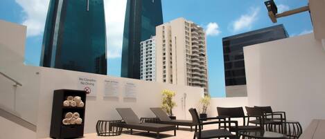 A rooftop terrace with lounge chairs, a small table, and a sign indicating pool rules.