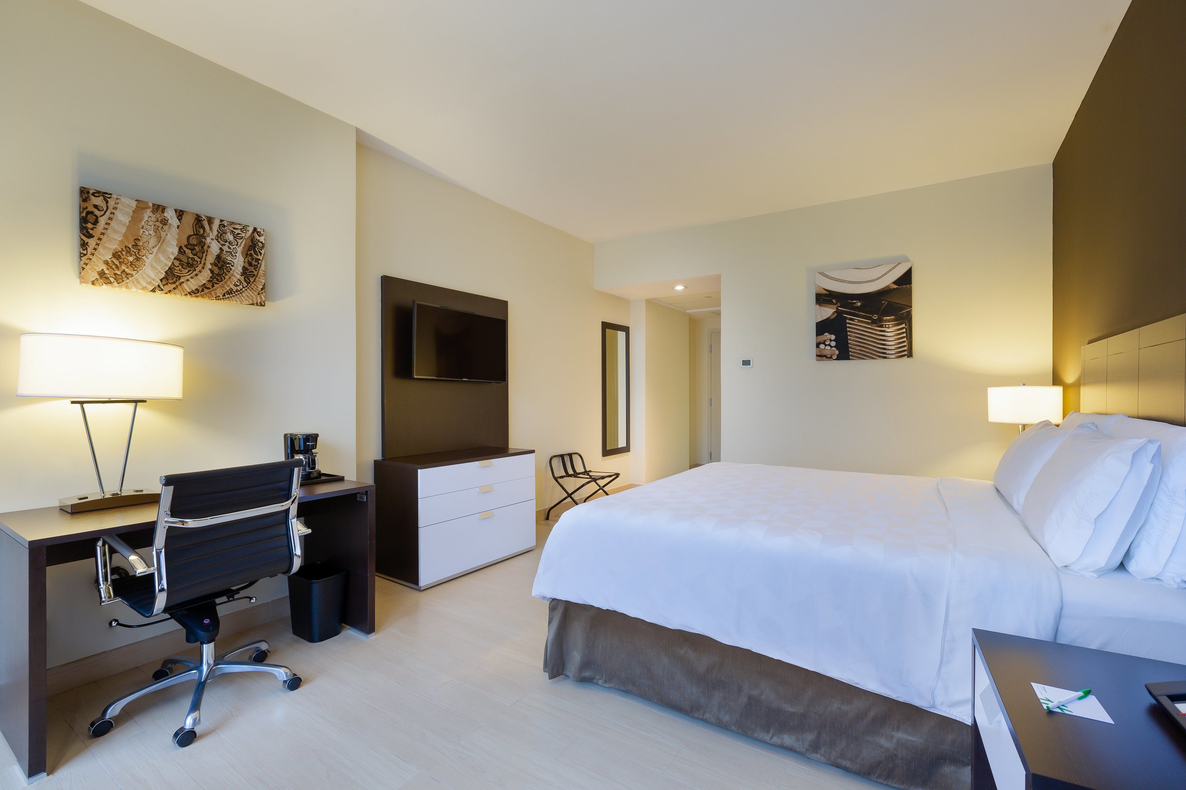 A hotel room with a bed, desk, chair, and a TV.