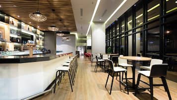 A modern bar area with a long counter, multiple hanging pendant lights, and a seating area with tables and chairs.