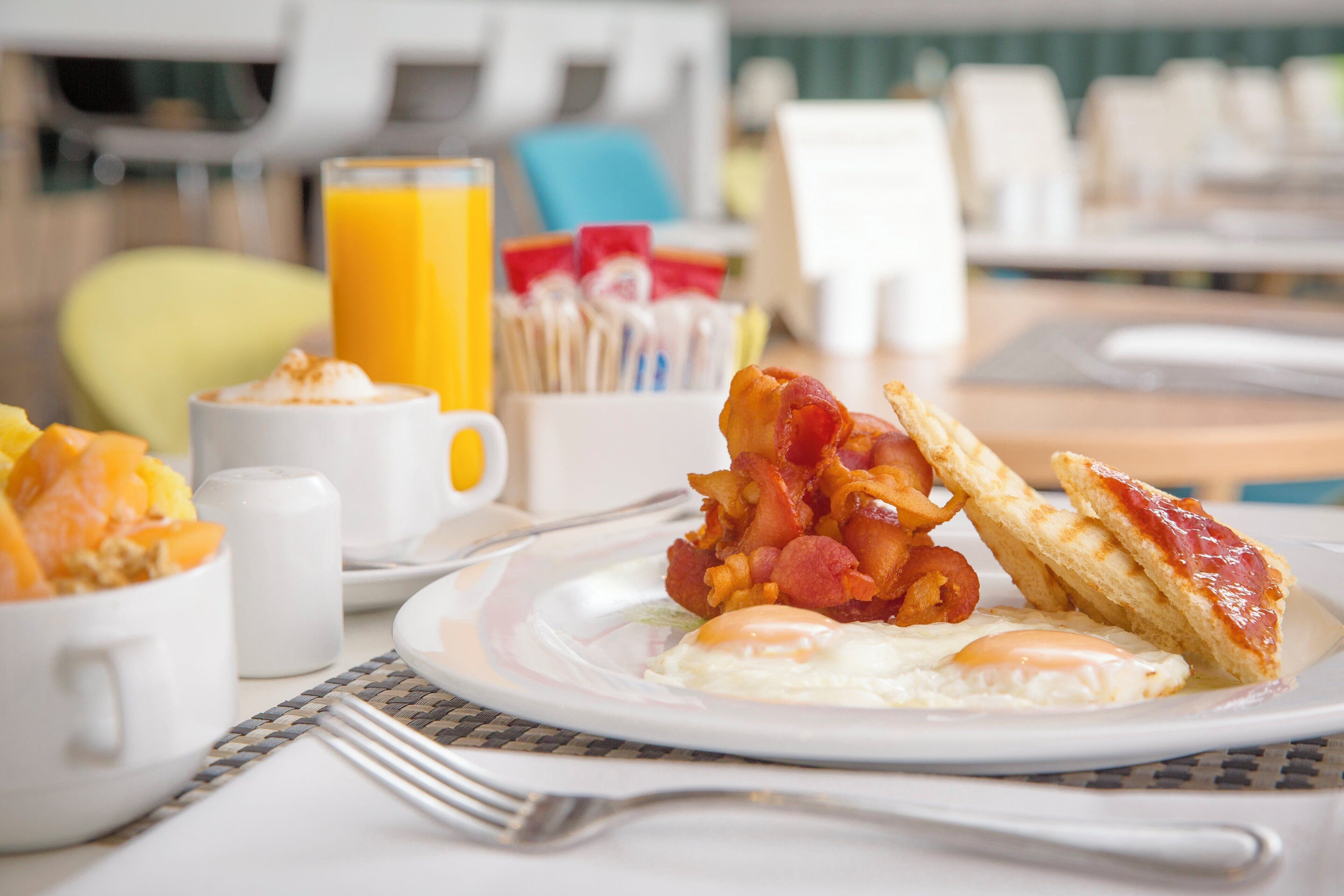 A breakfast setting with eggs, bacon, toast, and orange juice.