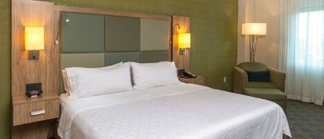 Una habitación de hotel con una cama grande, dos mesitas de noche, una silla y una lámpara.