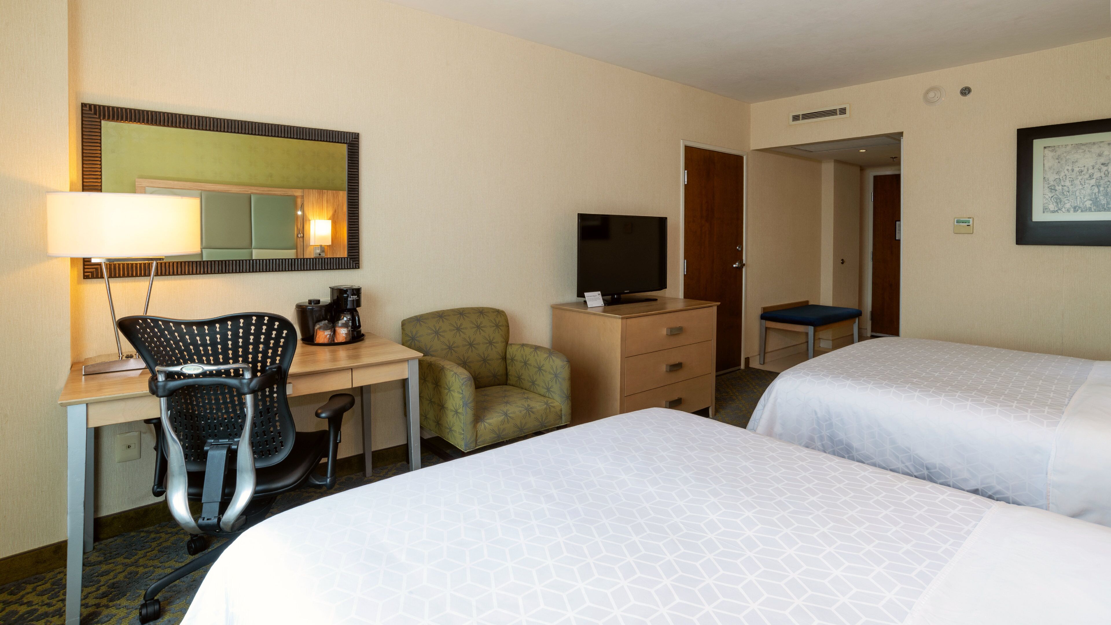 A hotel room with two beds, a desk with a chair, a television, and a small table.