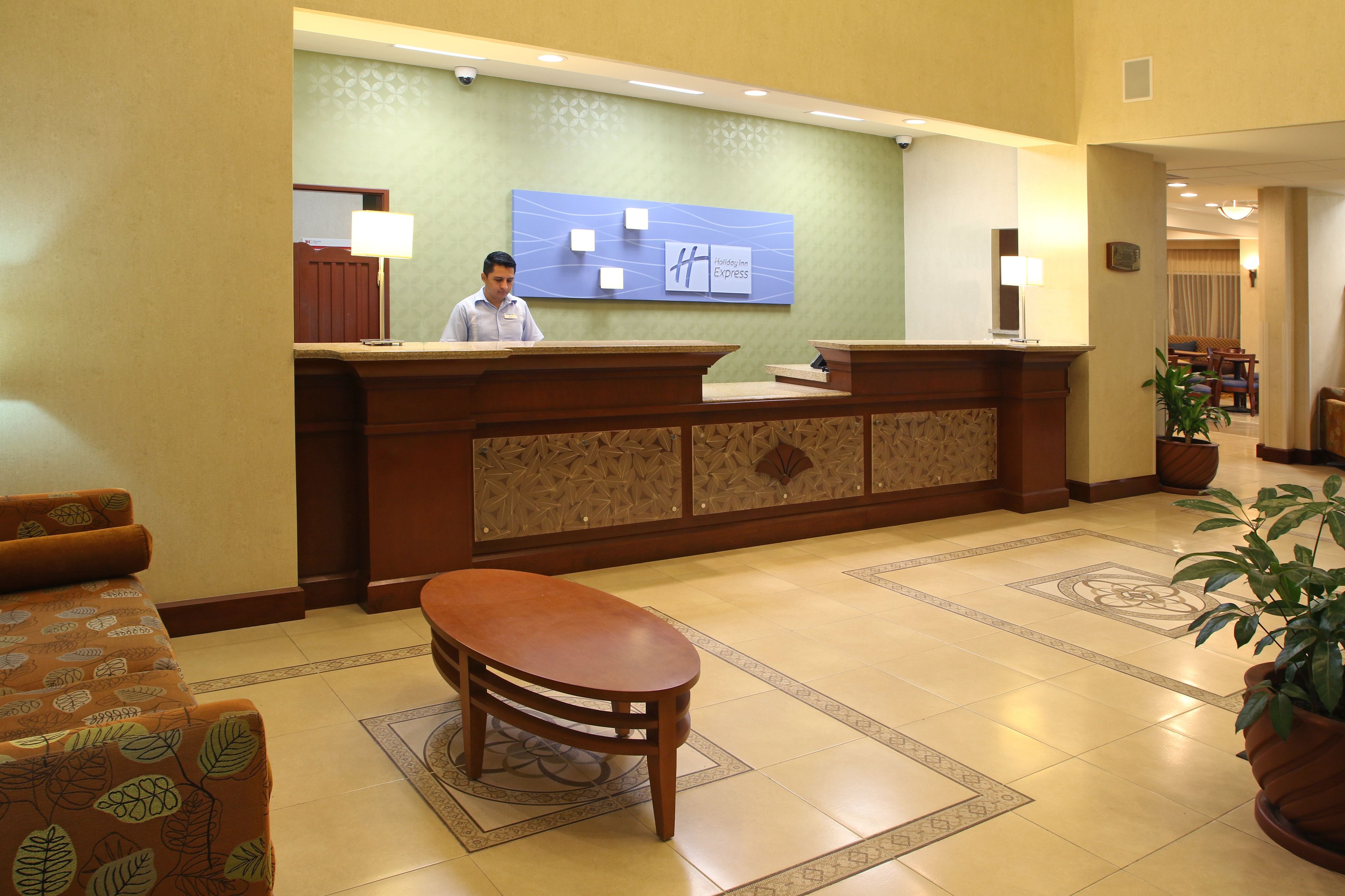 Zona de recepción de hotel con mostrador de madera, un espacio de estar con sofás estampados y una pared decorativa con un cartel.