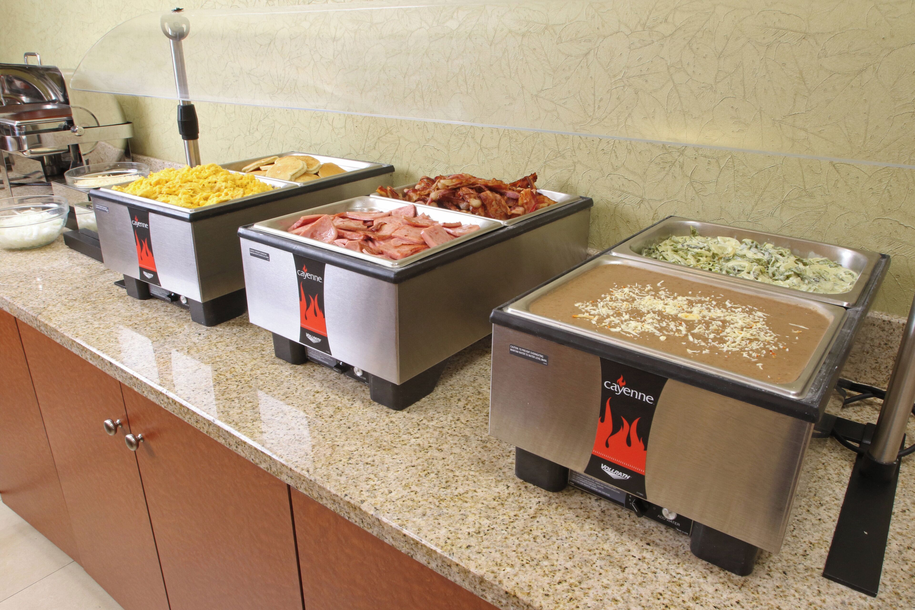 A buffet with various food options including scrambled eggs, bacon, and a pasta dish.
