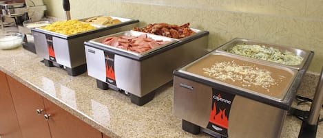 A buffet with various food options including scrambled eggs, bacon, and a pasta dish.