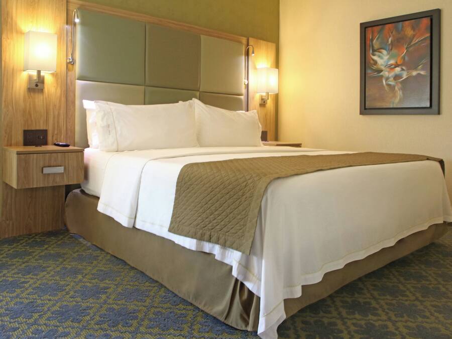 Quarto de hotel com cama, mesas de cabeceira, luminária na parede e um quadro.