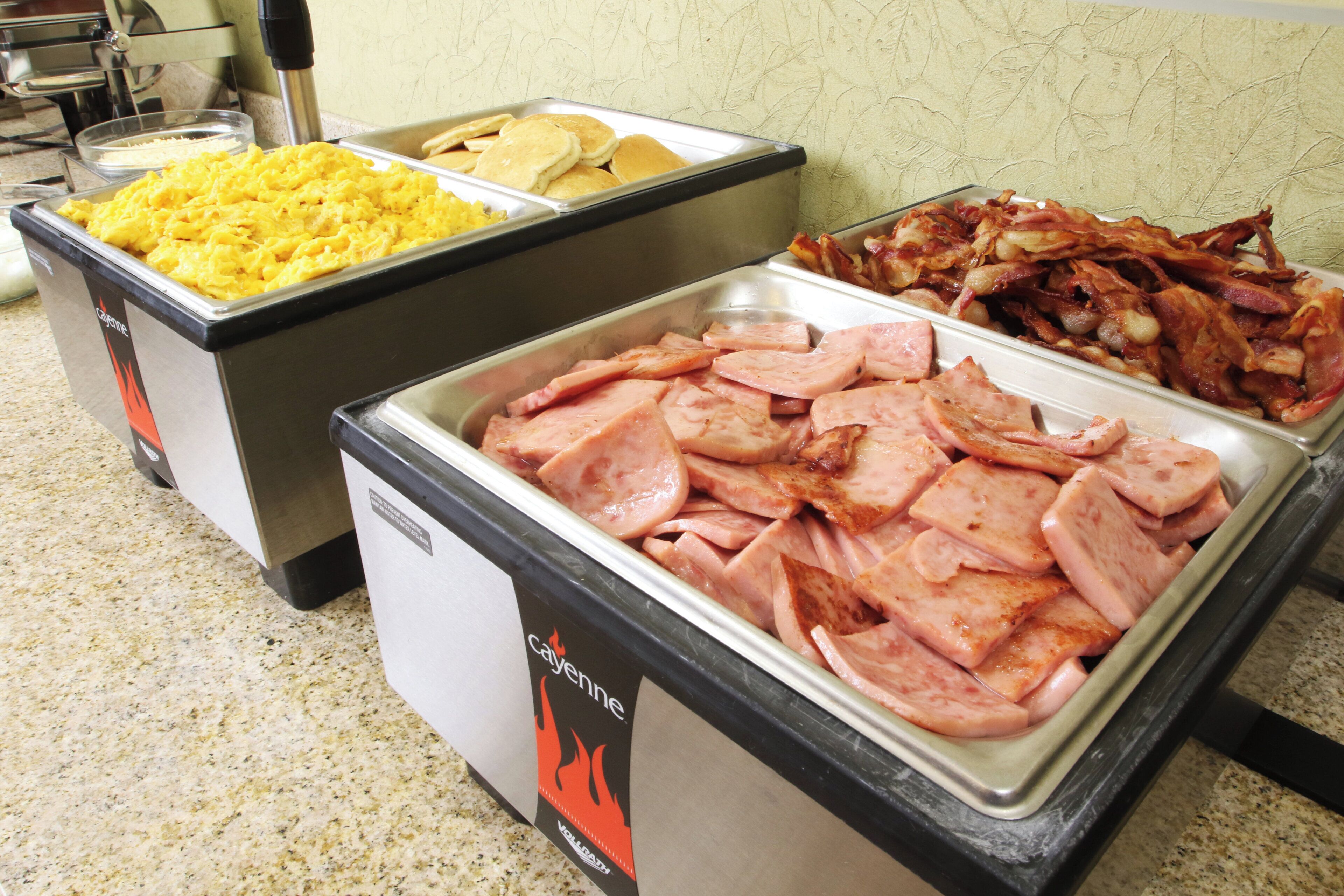A buffet with various food options including scrambled eggs, bacon, and sliced ham.