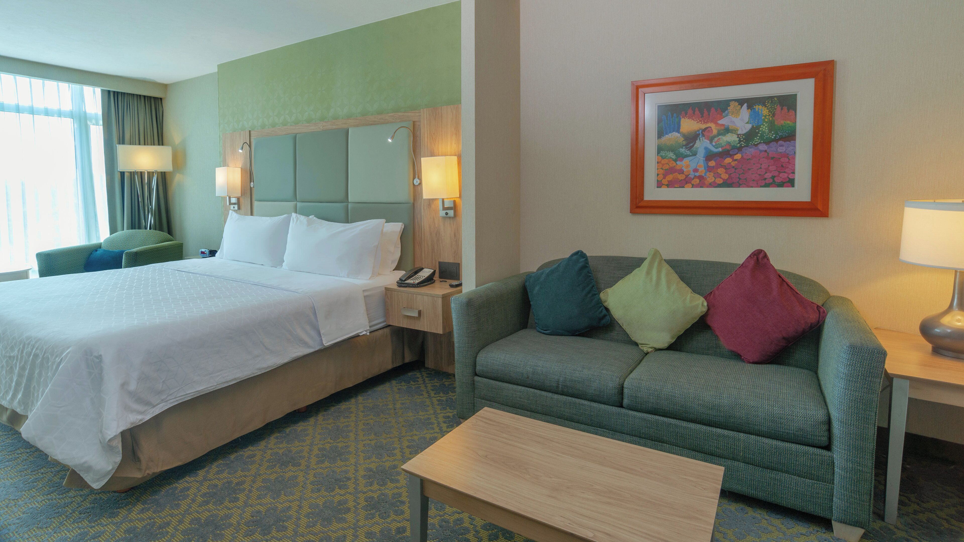 A hotel room with a bed, a sofa, a coffee table, and a painting on the wall.
