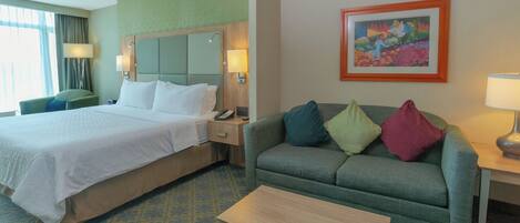 A hotel room with a bed, a sofa, a coffee table, and a painting on the wall.