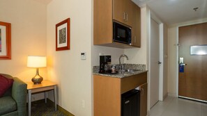 A compact hotel room with a kitchenette, a small table with a lamp, a framed picture on the wall, and a door with a sign. - Holiday Inn Express Hotel & Suites Cuernavaca by IHG (Cuernavaca)
