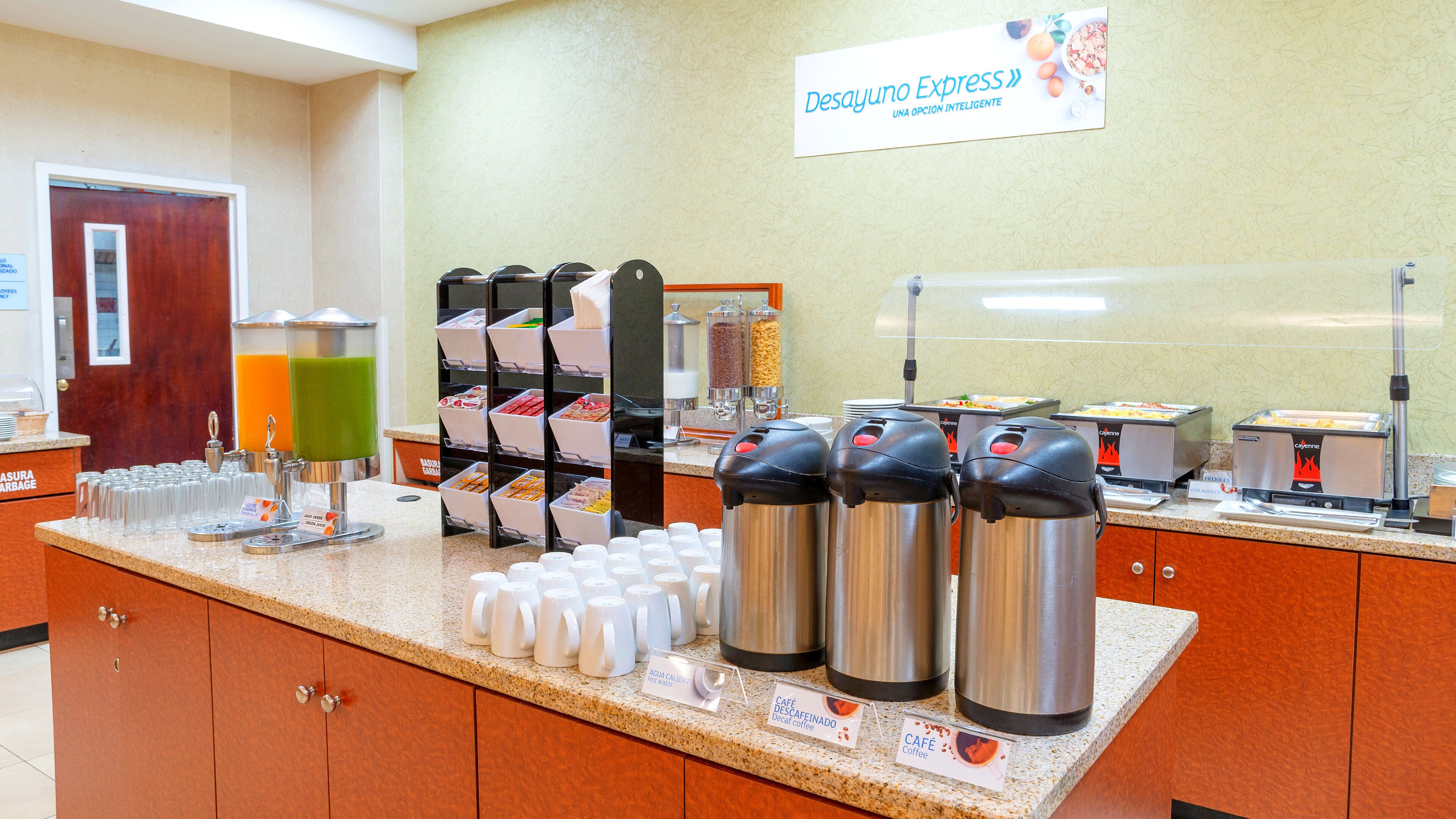 Un bar où l’on peut prendre le petit-déjeuner, avec des distributeurs de café et de jus de fruits, un buffet à salades et une enseigne indiquant « Desayuno Express ».