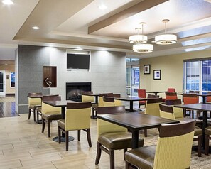 A spacious dining area with multiple tables and chairs, a fireplace, and large windows providing natural light. - Comfort Suites Minot South (Minot)