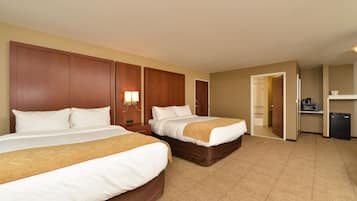 A hotel room with two beds, a desk, a mirror, and a small kitchenette.