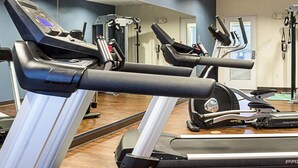 Et fitnesscenter med løbebånd og træningsudstyr, et spejl på væggen og en dør i baggrunden.