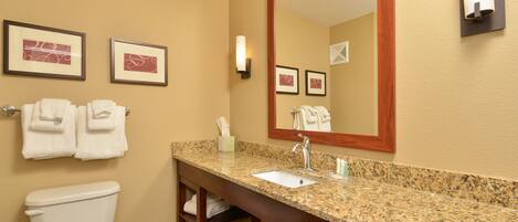 Un baño con inodoro, lavabo y espejo. Hay toallas colgadas en la pared y un cuadro enmarcado sobre el lavabo.
