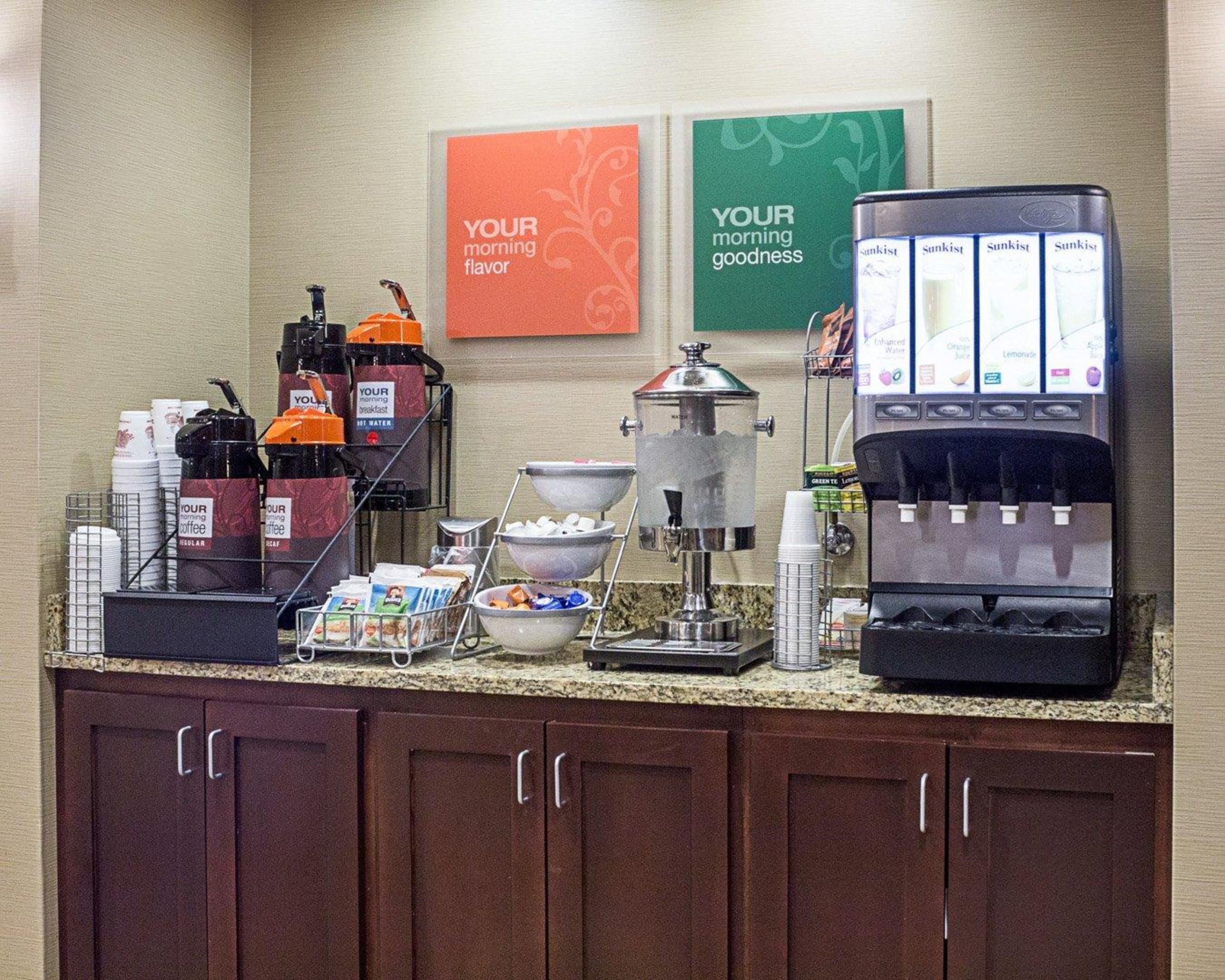 Espaço de café da manhã em hotel, com máquinas de café, dispensador de água e estação de café.