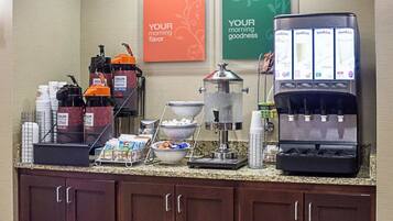 Espaço de café da manhã em hotel, com máquinas de café, dispensador de água e estação de café.