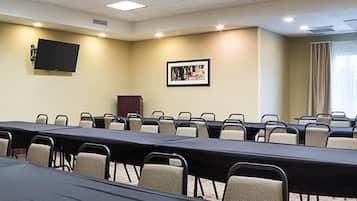 Uma sala de conferências com uma mesa comprida, cadeiras, uma televisão montada, um quadro emoldurado e um pódio.