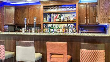A bar area with wooden cabinets, a variety of liquor bottles, and three patterned bar stools.