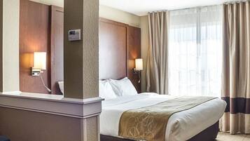 A hotel room with a large bed, two bedside lamps, a nightstand, and a window with curtains.