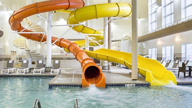 Et vandland med flere rutsjebaner i orange og gul, indendørs pool, liggestole og en trappe.