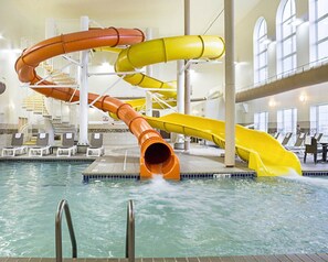 A water park with multiple slides in orange and yellow, indoor pool, lounge chairs, and a staircase.