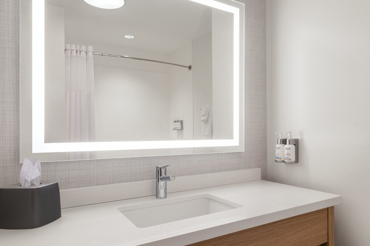 A modern bathroom with a large mirror, a white sink, and a towel rack.