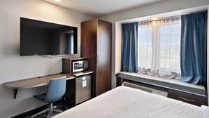 A hotel room with a bed, a desk with a chair, a microwave, a TV, and a window with curtains. - Garner Hotel Gonzales by IHG (Gonzales)