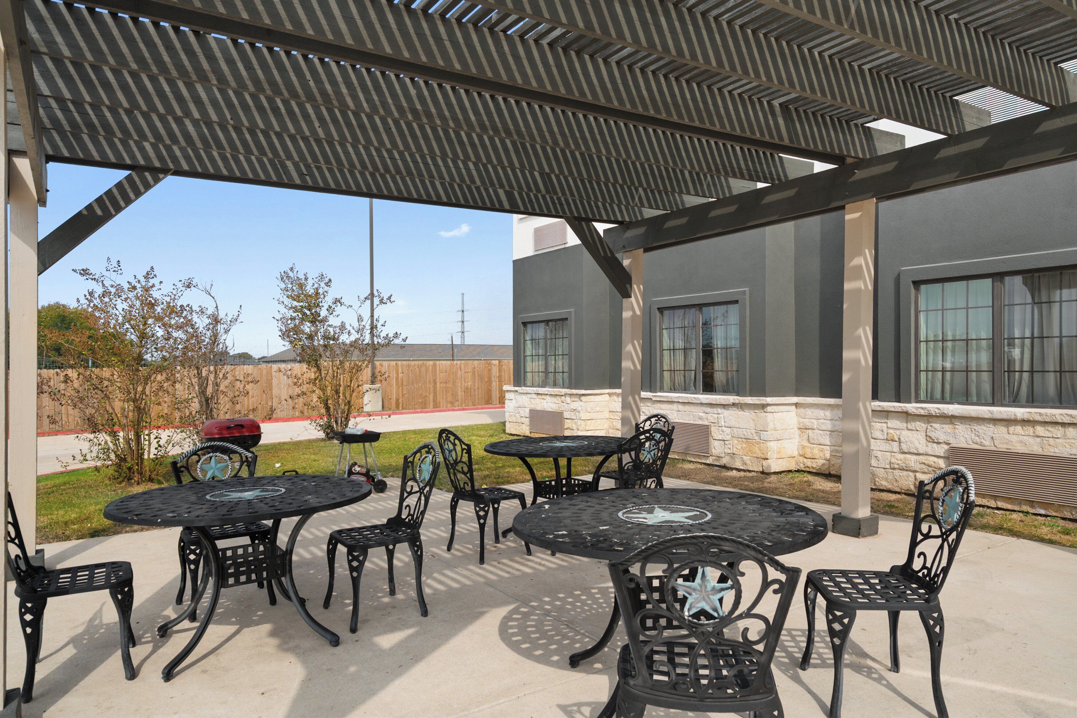 An outdoor patio with metal tables and chairs, a covered area, and a view of a building with large windows.
