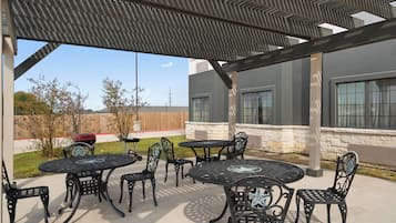 An outdoor patio with metal tables and chairs, a covered area, and a view of a building with large windows.