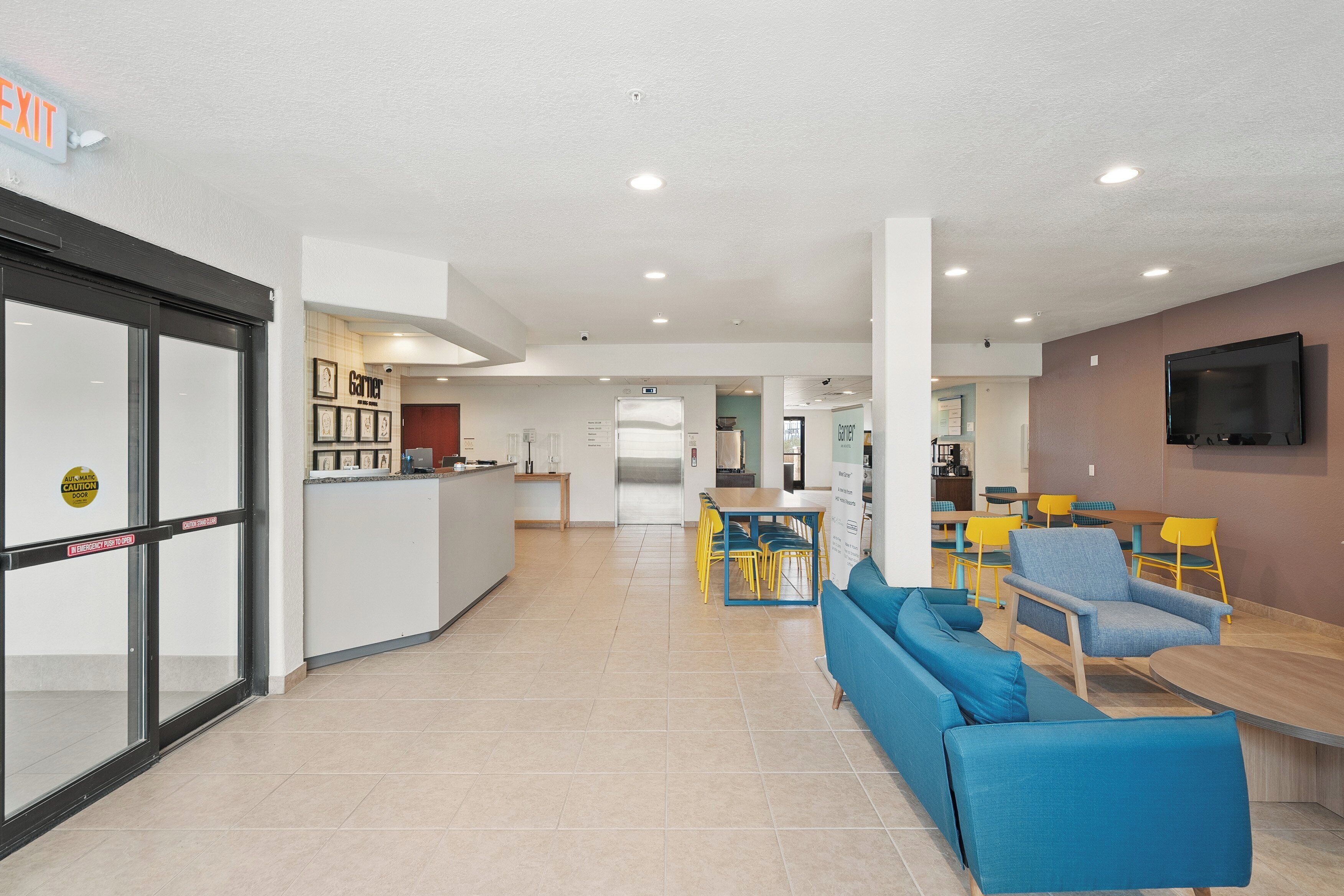 Een modern interieur met een receptiebalie, een eetgedeelte met gele stoelen en een zithoek met blauwe banken.