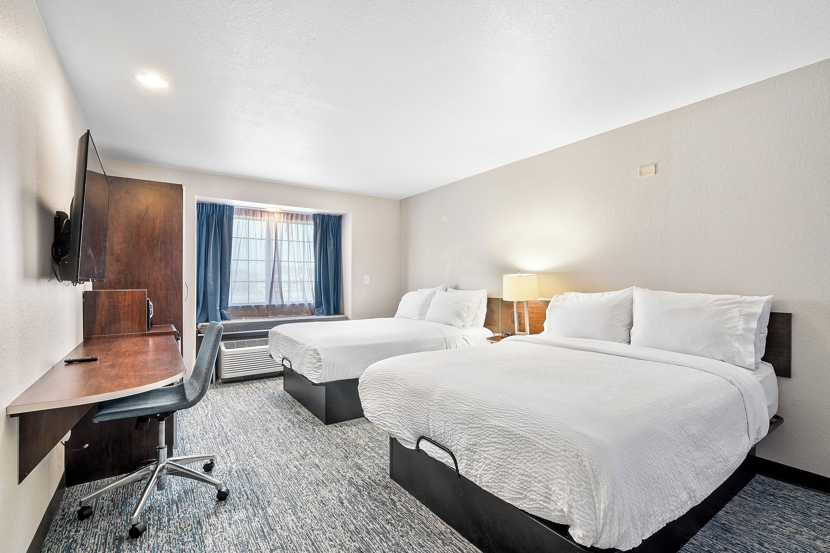 A hotel room with a desk, two beds, a TV, and a window with curtains.
