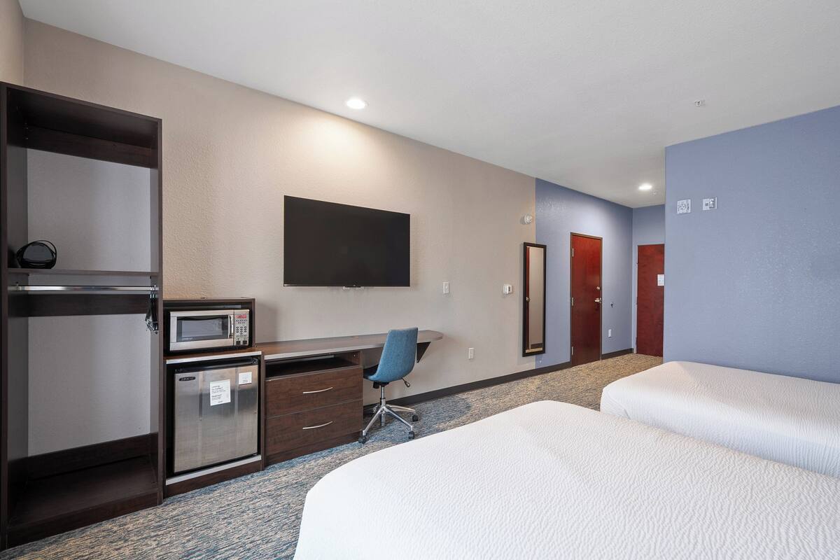 A hotel room with a bed, a desk with a microwave, a chair, and a TV mounted on the wall.