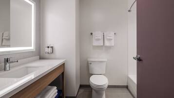 A modern bathroom with a white sink, mirror, and toilet. There are towels hanging on a rack and a shower curtain visible.