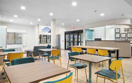 A modern dining area with tables and chairs, a kitchen area, and a visible exit sign.