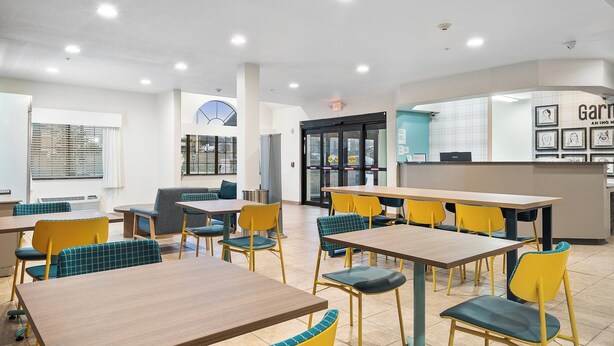 A modern dining area with tables and chairs, a kitchen area, and a visible exit sign. - Garner Hotel Gonzales by IHG (Gonzales)