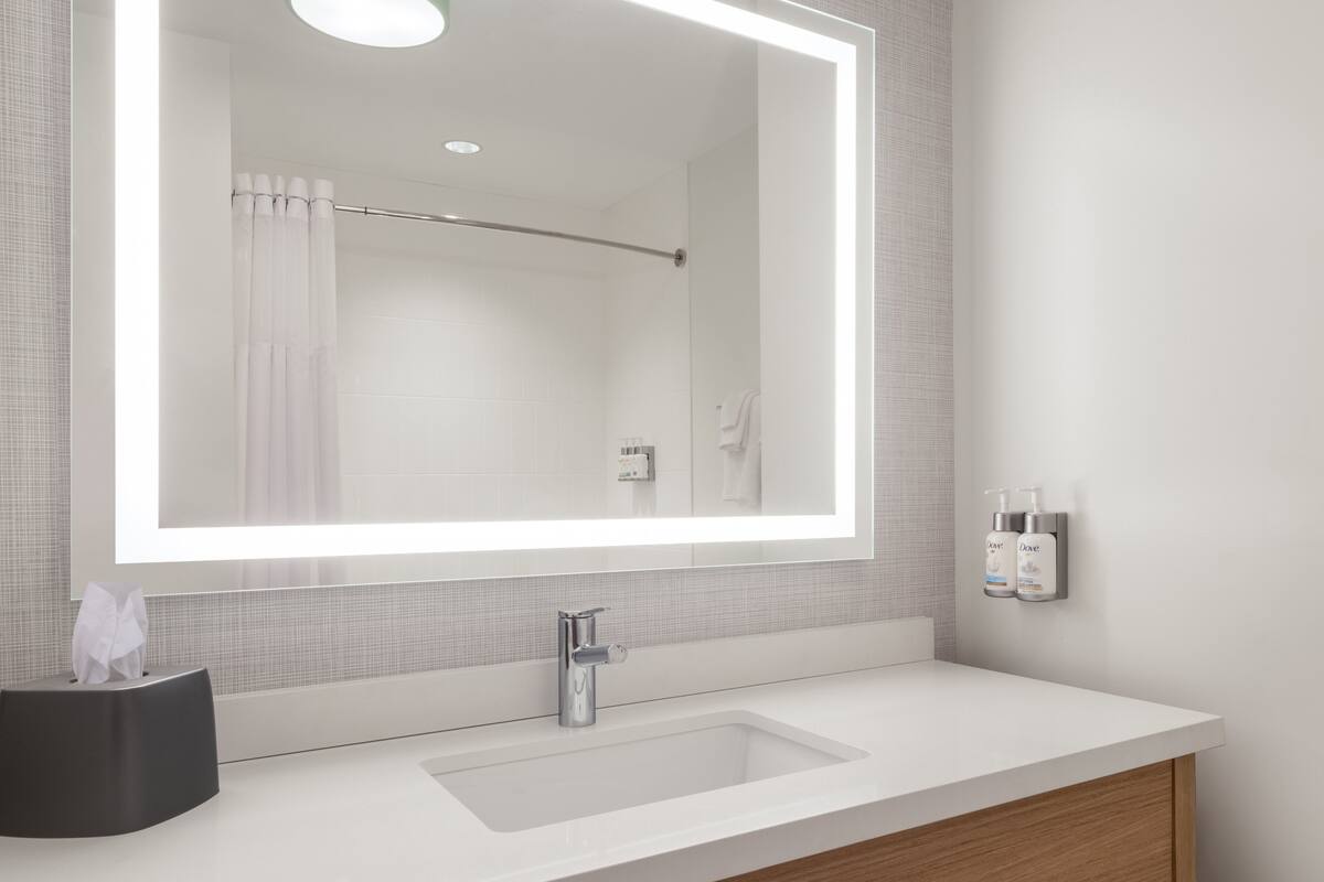A modern bathroom with a large mirror, a white sink, and a towel rack.